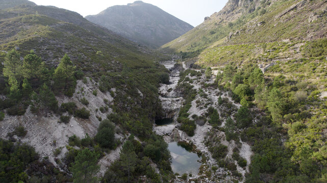 Aerial view of the natural pools of Pocos Verdes surrounded by rocky mountain slopes, pine forests, and a winding stream in Cabril, Vila Real, Portugal.