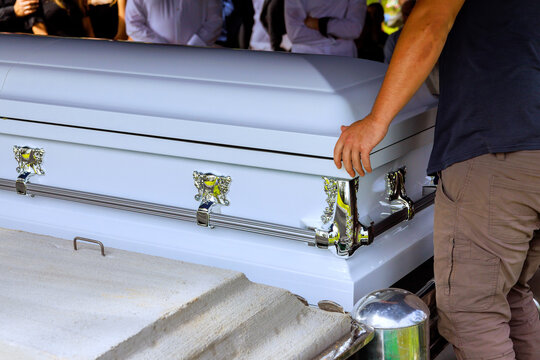 Ceremony taking place with coffin being lowered at burial site in cemetery