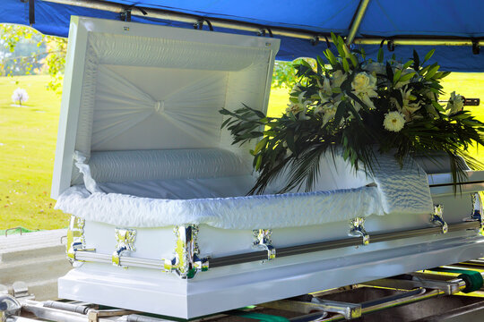 Coffin with flowers placed in graveyard under blue canopy during burial ceremony