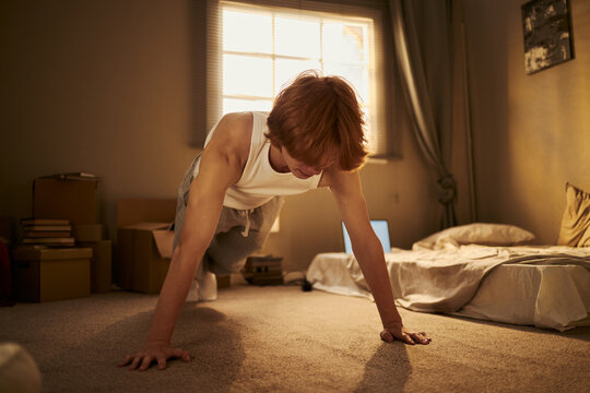 Caucasian young adult man doing pushups on floor in apartment during home workout routine. Suitable for fitness app promotion, wellness editorial, or daily exercise lifestyle campaigns