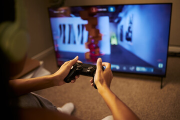Close up of multi-ethnic young adult woman holding wireless gamepad controller playing video game on television screen. Image suitable for digital entertainment advertising © DragonImages
