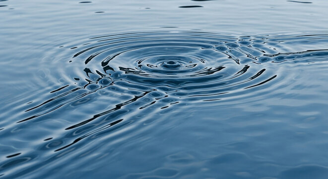 A series of gentle concentric circles expand across the surface of the deep blue liquid after a single drop impacts the calm fluid creating motion that radiates outward in a natural flowing