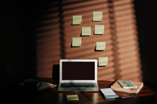 Laptop, sticky notes, notebooks on minimal home office desk, sunlight shadows, copy space