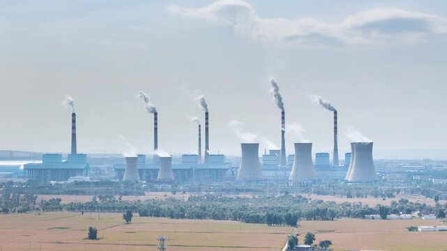 Aerial time-lapse of cooling towers and tall chimneys emitting white steam at a coal-fired power plant in Hohhot, Inner Mongolia, above hazy autumn farmland.
