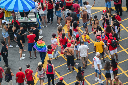 Rio de Janeiro, Brazil - 12 October 2026: Aerial view of a crowd gathered in the street during a political event in Copacabana, with people wearing red shirts and a rainbow flag.