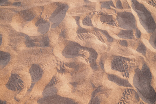 Footprints and shoe prints in warm golden sand at sunset, close-up natural texture background