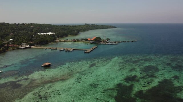 Aerial view of a tropical island harbor in Karimunjawa, Central Java, Indonesia, with a long pier, moored boats, coral reef and turquoise sea