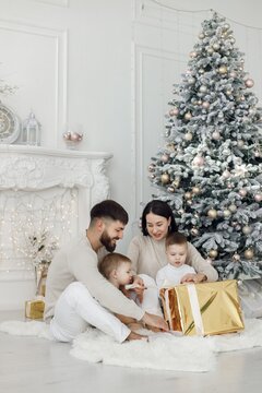 Young family in white clothes sitting near Christmas tree