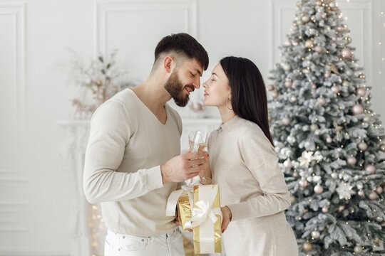 Romantic couple standing near Christmas tree with glasses of champagne