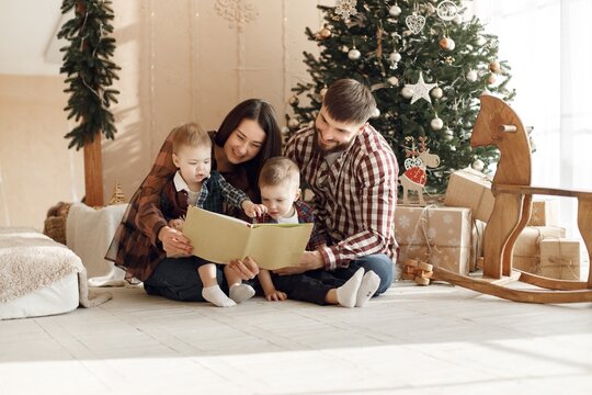 Young family in plaid shirts sitting near Christmas tree
