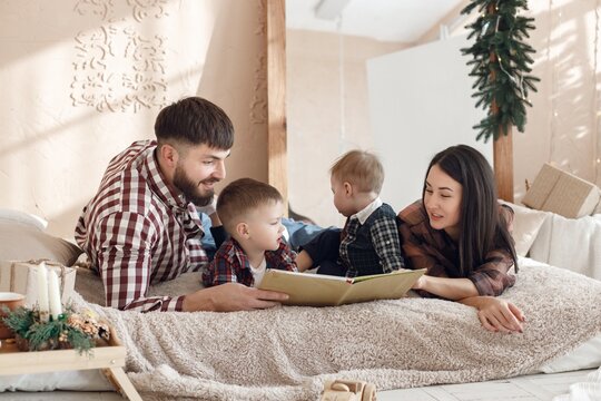 Young family in plaid shirts laying on a blanket and reading a book