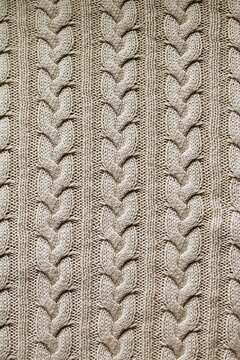 Vertical macro close-up of a warm beige woolen sweater featuring a traditional cable knit pattern and soft texture.