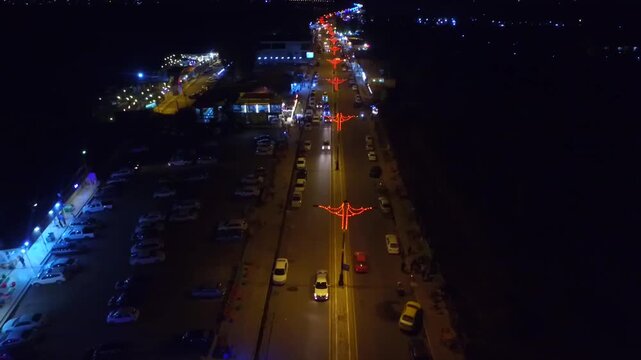 Night aerial of a lit boulevard with traffic and decorative lights near an amusement park, Mosul, Iraq