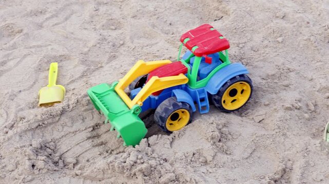 Colorful toy tractor with bucket sits partially buried in sand beside a small plastic castle mold