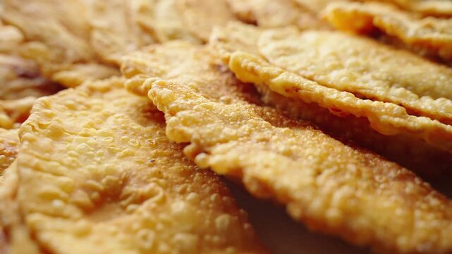 Golden, crispy, fried flatbreads pile neatly. Each crumbly, puffy surface shows perfect crispiness. Deep golden hue suggests rich, savory flavor. No people, just food's inviting, textured appeal