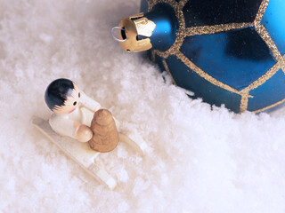 Fototapeta premium Wooden angel with blue Christmas bauble in snow
