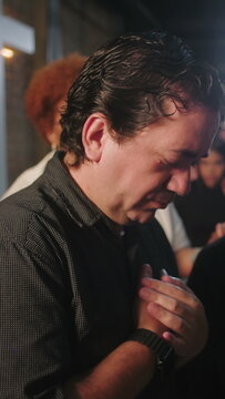 Mature Hispanic man holding hands over heart with closed eyes in deep prayer and emotional devotion during indoor church worship service