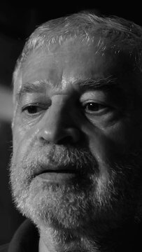 Senior white person looking away thoughtfully in dark studio reflecting on wisdom aging memory contemplation experience resilience vulnerability solitude dementia and nostalgia