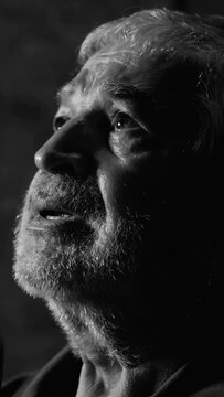 Black and white photo of senior elderly man placing hands over heart with deep emotion and sorrow during indoor church worship service