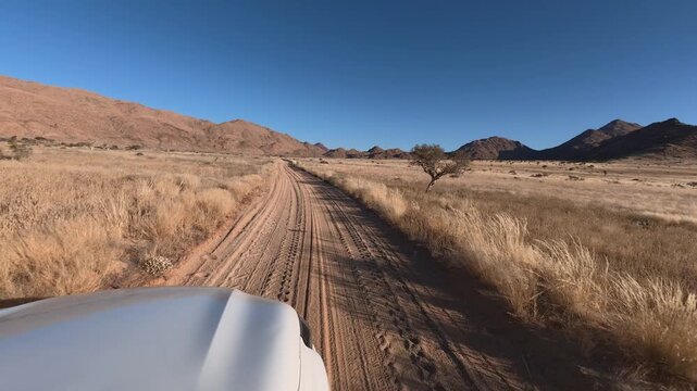 A solitary white car drives along a gravel dirt road in Namibia, Africa