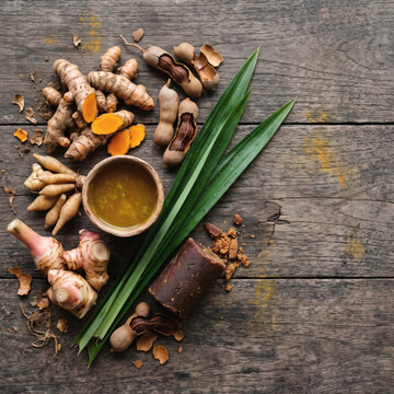 Overhead view of traditional Indonesian jamu ingredients with turmeric, galangal, tamarind, and palm sugar on a weathered teak table
