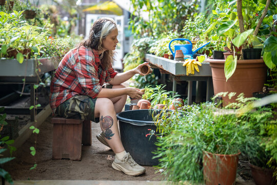 Responsible thoughtful woman florist working in greenhouse, sitting washing old inventory pots in basin, pensive serious female botanist cleaning ceramic flower pots in bucket with water and sponge.