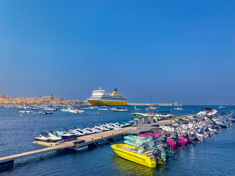 L'Ile-Rousse, Corsica, France, July 27, 2026: port of with large yellow Corsica Ferries passenger ship docked at pier, with rental jet skis and small motorboats lined up on floating dock.