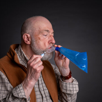 Head and shoulders portrait of a senior man performing breath test to diagnose SIBO (small intestinal bacterial overgrowth)