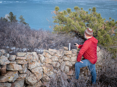 senior hiker taking rest at old stone fence and looking at frozen Horsetooth Reservoir