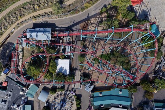 Aerial view of a red roller coaster track winding through an amusement park with surrounding pathways and structures in Denver, Colorado, United States.