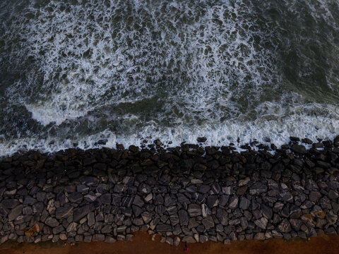 Aerial view of waves crashing against a rocky shoreline with large dark stones in Ghana.
