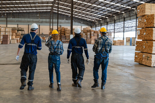 Four workers demonstrate factory teamwork as they walk away from a team meeting through the warehouse beside stacked lumber.