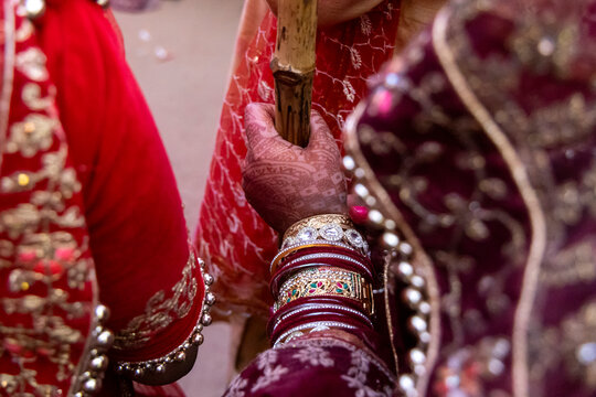 Close up of a henna decorated hand holding a stick among red and maroon embroidered saris, Barsana, India