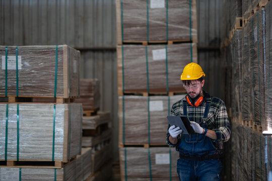 Checking export packaging during inspection, a man uses a tablet to review an export shipment among stacked wrapped pallets.