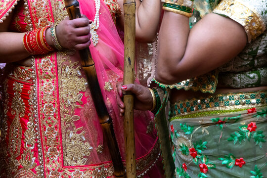 Close up of women in red and pink embroidered saris holding bamboo sticks at Lathmar Holi, Barsana, India