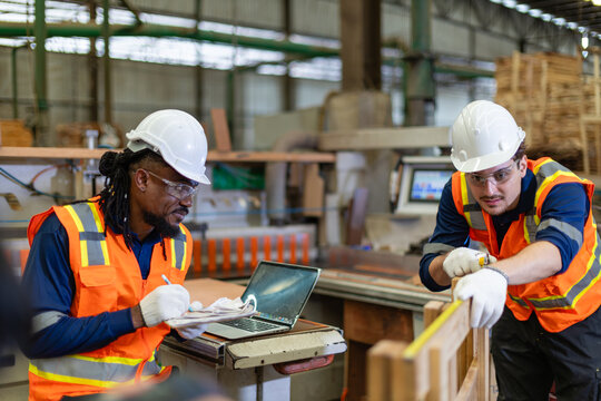 Measuring plywood for woodworking, a carpenter checks a wooden frame while his male colleague writes on a clipboard.