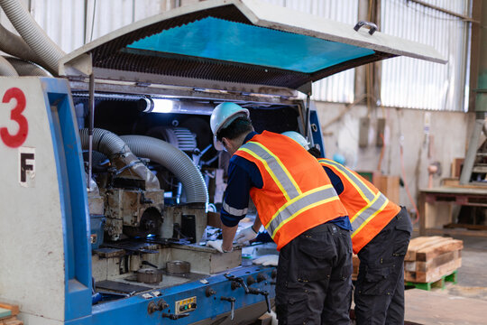 A technician performing machine maintenance and a colleague inspect the open woodworking moulder beside stacked wood.