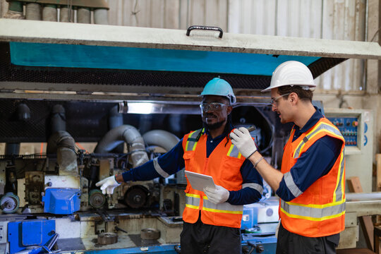 During machine maintenance, a technician points inside an open moulder while his colleague illuminates its components with a flashlight.