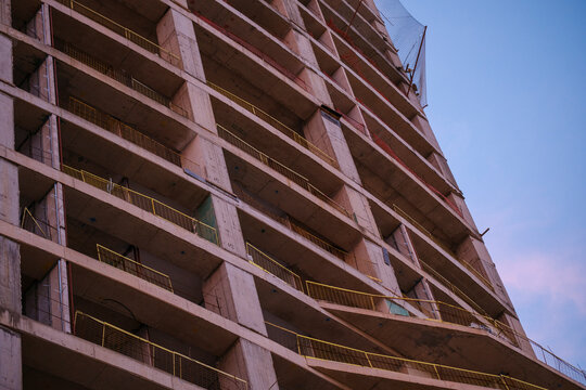 Low angle view of unfinished multistorey concrete residential building frame with safety nets during evening urban construction process