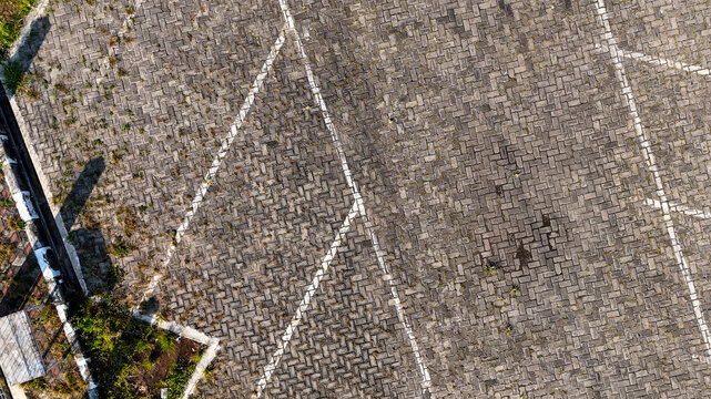Aerial view of the paved parking area at Karimunjawa Passenger Ferry Port with white painted lines and patches of weeds in Karimunjawa, Central Java, Indonesia.