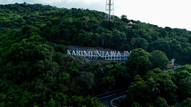 Aerial view of the Karimunjawa sign nestled on a lush, forested hillside with a communication tower in the background in Karimunjawa, Central Java, Indonesia.