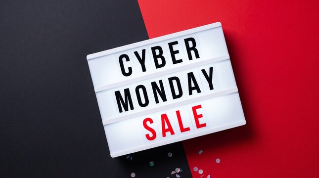 A bright lightbox sign displays CYBER MONDAY SALE in white and red text, set against a bold black and red background. Small clear particles are scattered across the surface below the sign
