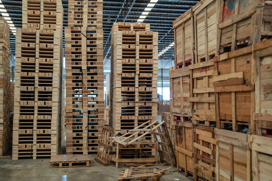 Wooden pallets form a warehouse pallet stack in an empty storage area beside large wooden crates and broken wood.