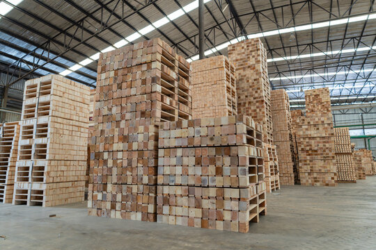 Filling a lumber warehouse, timber pallets form tall rows beside stacked lumber and piles of solid rectangular wood blocks.