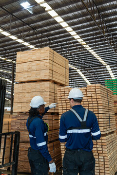During lumber inventory checks, warehouse colleagues stand together as a man points toward a tall stack of sawn timber.