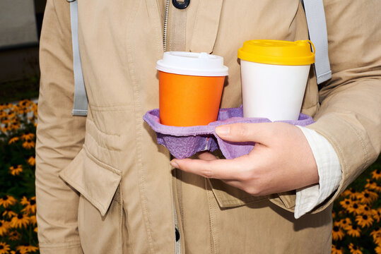 Person holding two coffee cups in city park