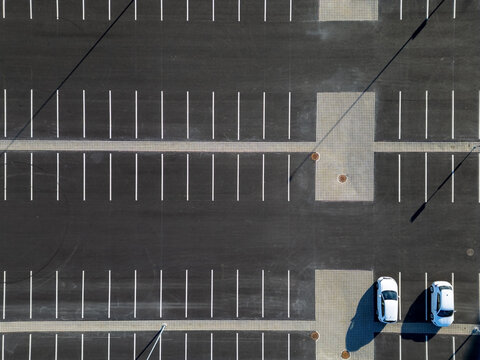 Aerial view of a parking lot with white painted lines on asphalt surface and two white cars parked in Oulu, North Ostrobothnia, Finland.