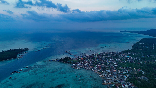 Aerial view of Karimunjawa island with turquoise waters, coral reefs, a coastal village, and small boats scattered in the bay in Karimunjawa, Central Java, Indonesia.