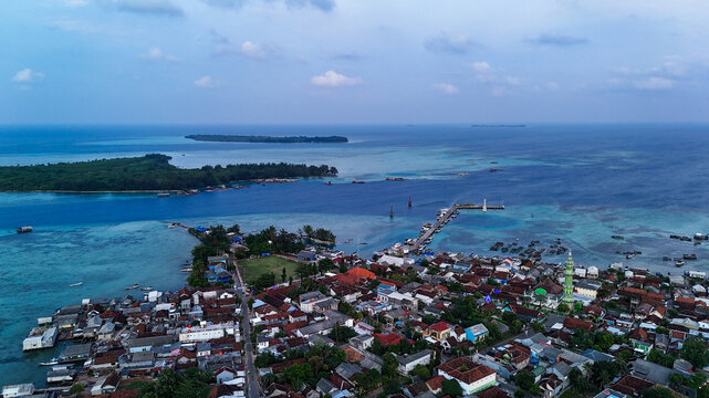 Aerial view of Karimunjawa town with a mosque, dense rooftops, and a pier extending into the turquoise waters of the Java Sea in Karimunjawa, Central Java, Indonesia.