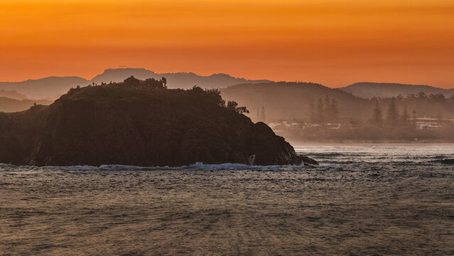Aerial view of Norries Headland at Cabarita Beach with waves crashing against the rocky shore under a vibrant orange sunset sky in Cabarita Beach, New South Wales, Australia.